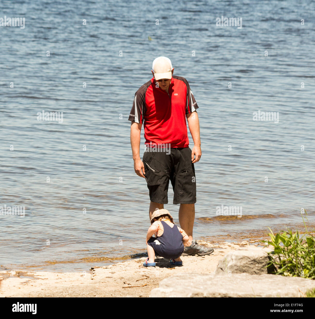 Homme et enfant sur la plage toddler pokes dans le sable. Banque D'Images