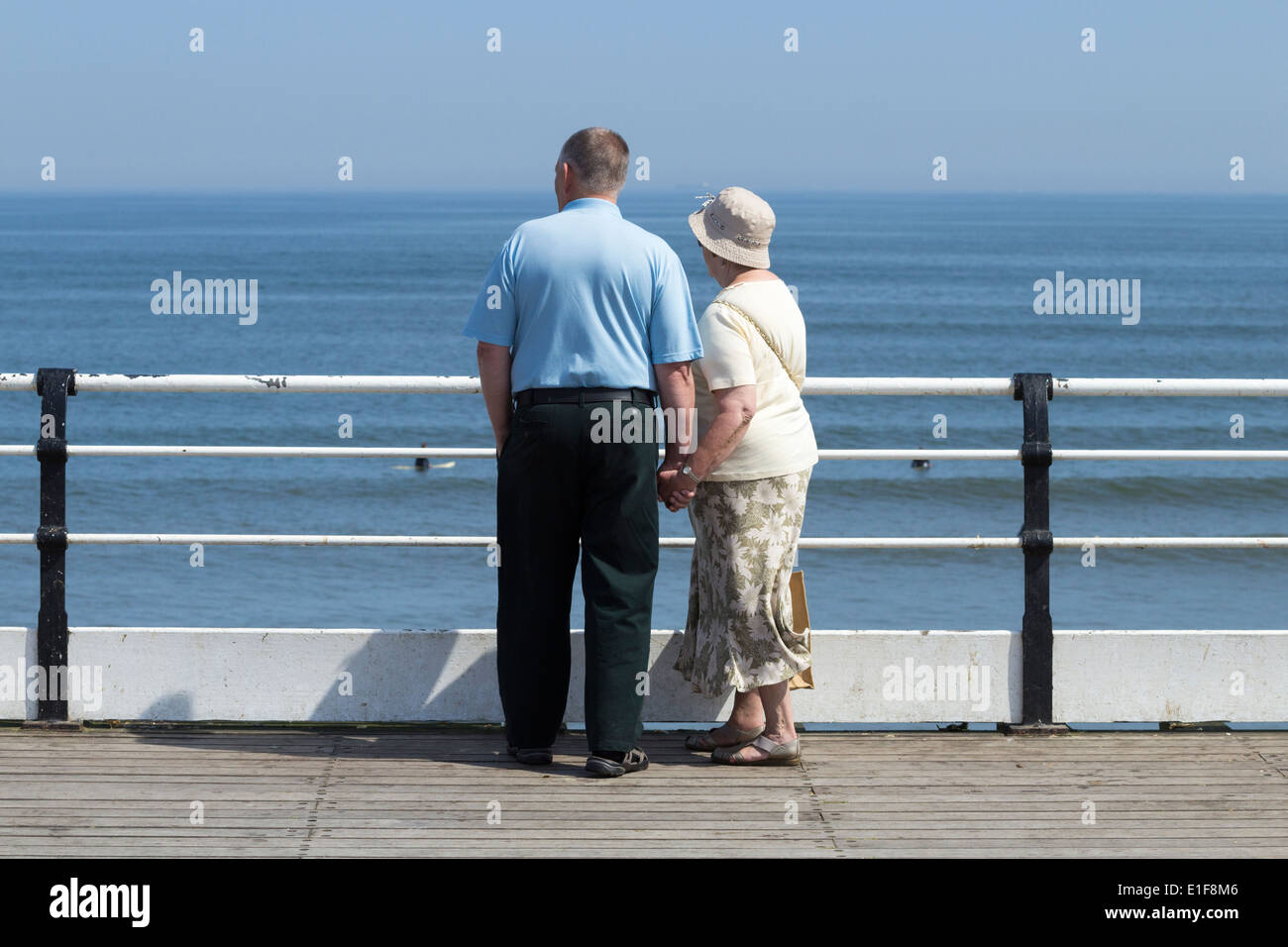 Vieux couple holding hands regarder les surfeurs de Saltburn's Victorian pier Banque D'Images