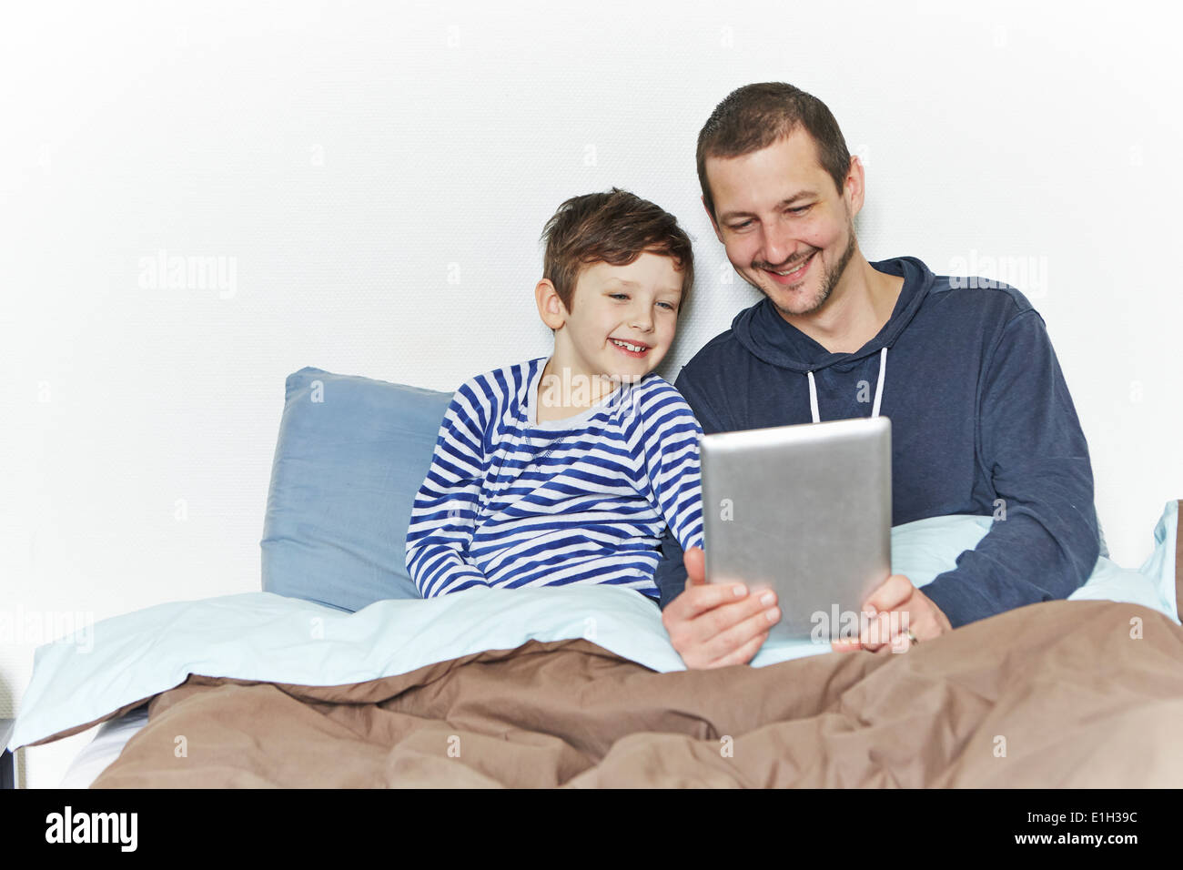 Père et fils using digital tablet in bed Banque D'Images