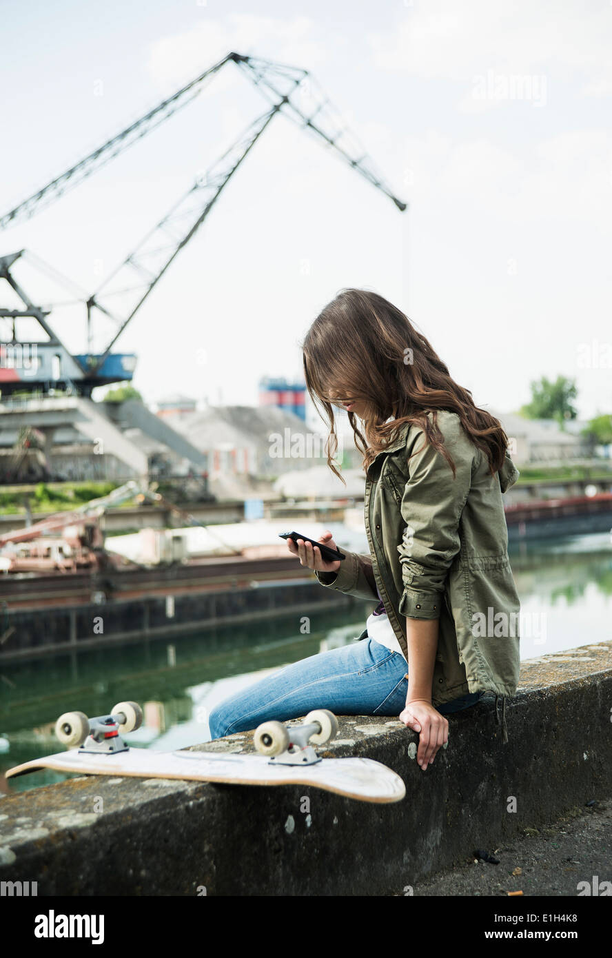 Young woman sitting on wall using cell phone Banque D'Images