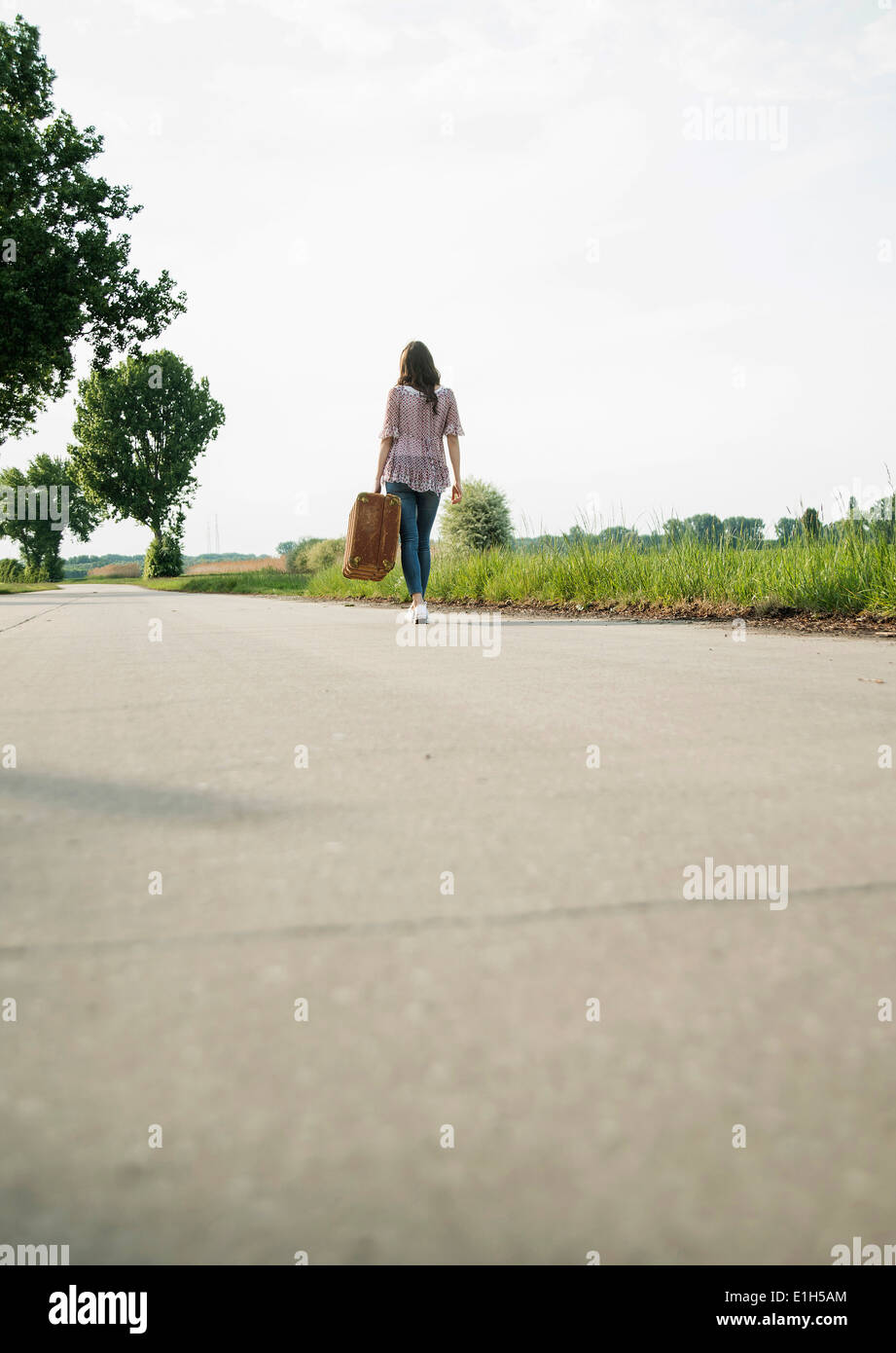 Young woman walking on country road réalisation suitcase Banque D'Images