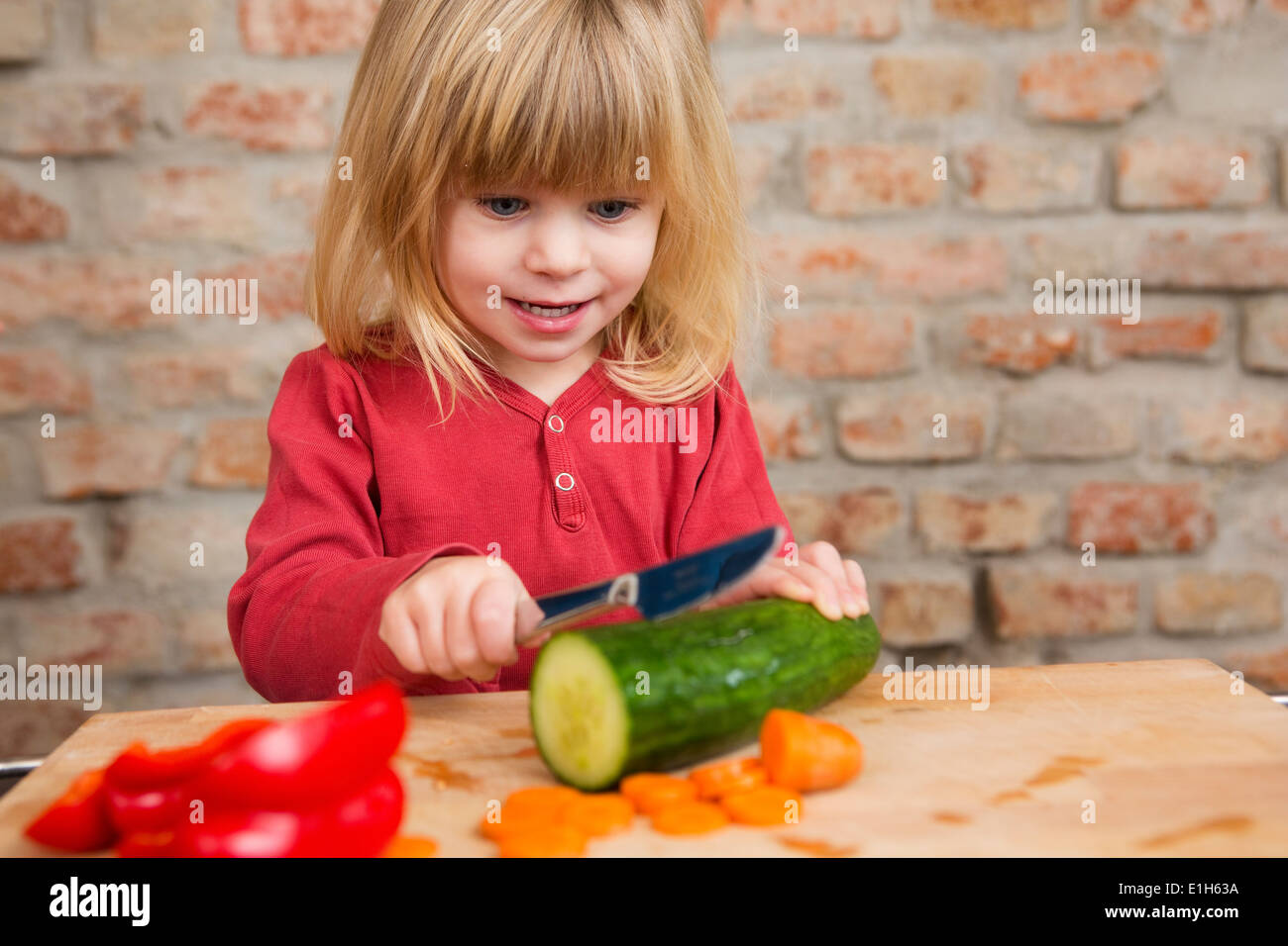 Fillette de deux ans dans l'apprentissage de la cuisine légumes coupe Banque D'Images