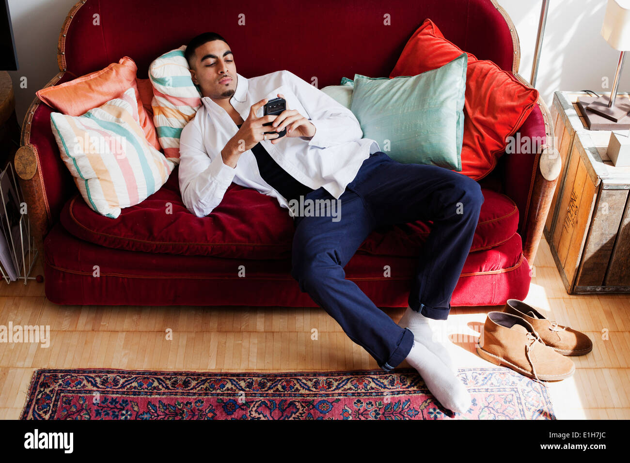 Young man lying on sofa, using smartphone Banque D'Images
