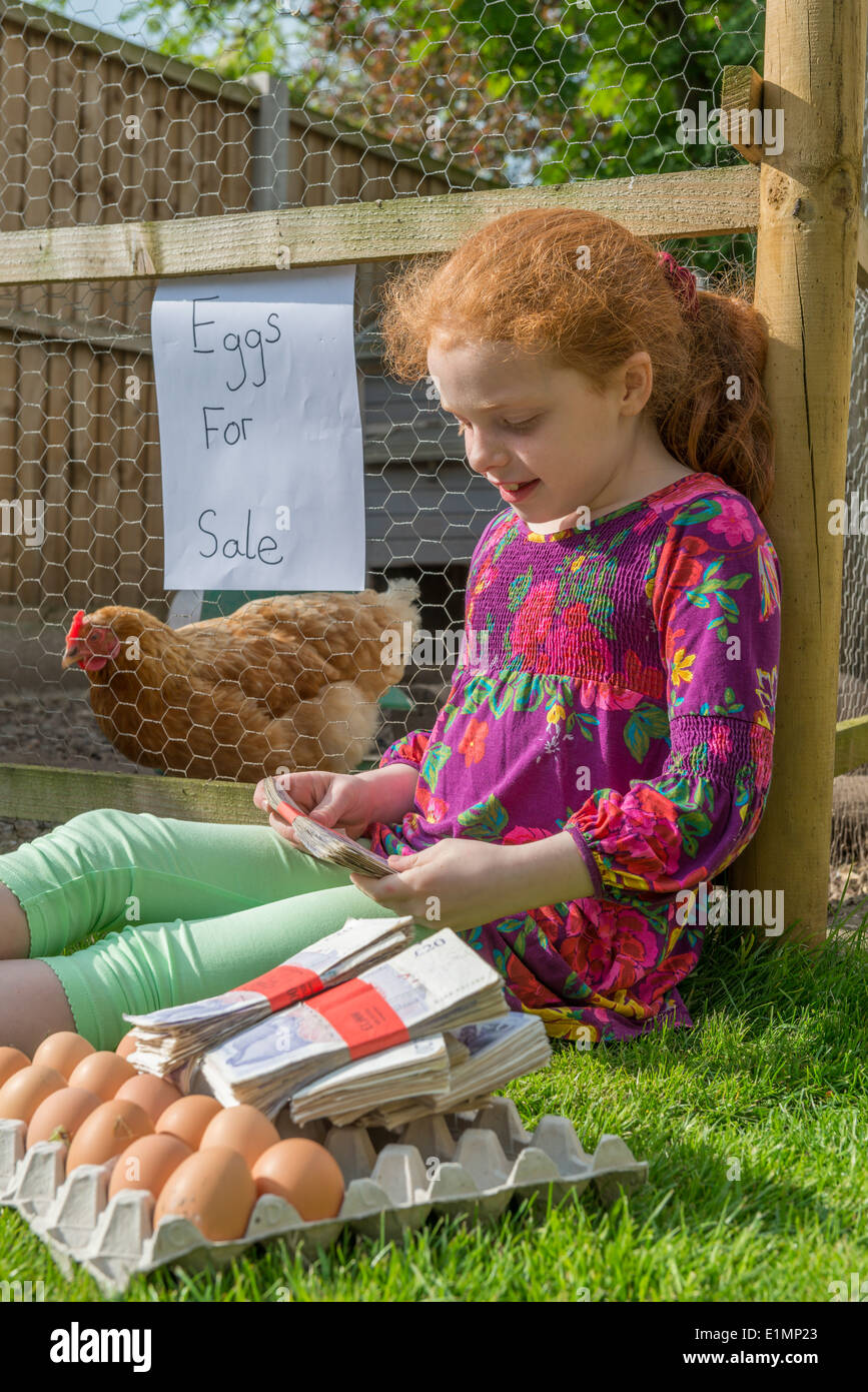 Petite fille entrepreneur siège avec des milliers de livres, tout en vendant des oeufs de poules. Banque D'Images
