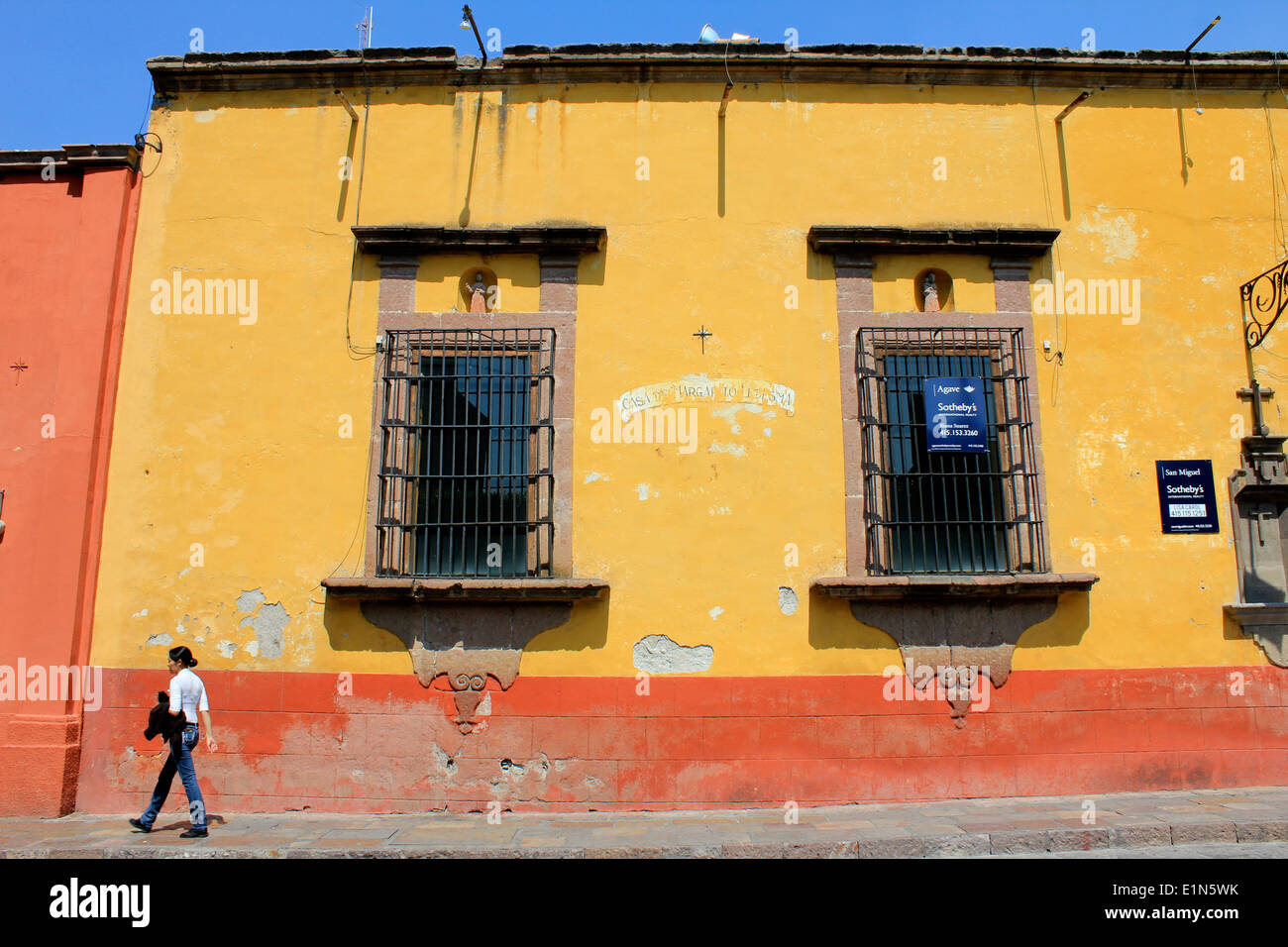 Bâtiment jaune et rouge avec fenêtres et une personne marchant le long de la rue, San Miguel de Allende, Guanajuato, Mexique Banque D'Images