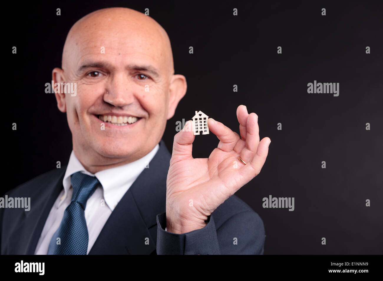 Un vieil homme sûr de lui sourire avec une petite maison de bois entre ses doigts Banque D'Images