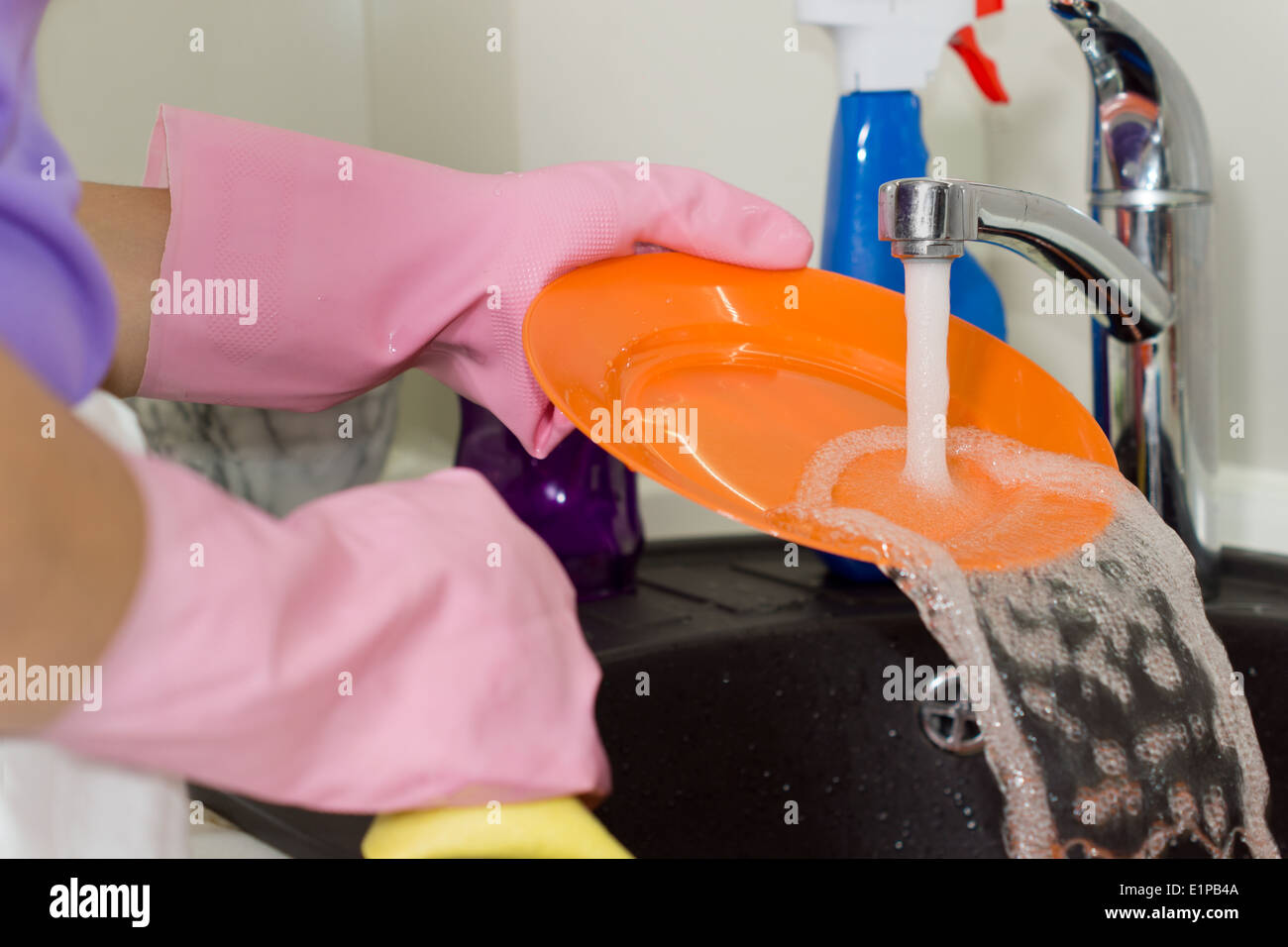 Rinçage de la femme d'un orange lumineux colorés plaque sous l'eau courante comme elle se lave la vaisselle dans l'évier de cuisine Banque D'Images