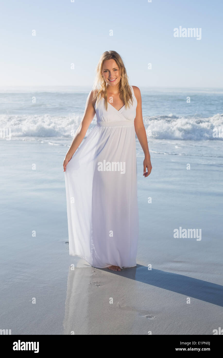 Jolie blonde smiling at camera à la plage en robe blanche Banque D'Images