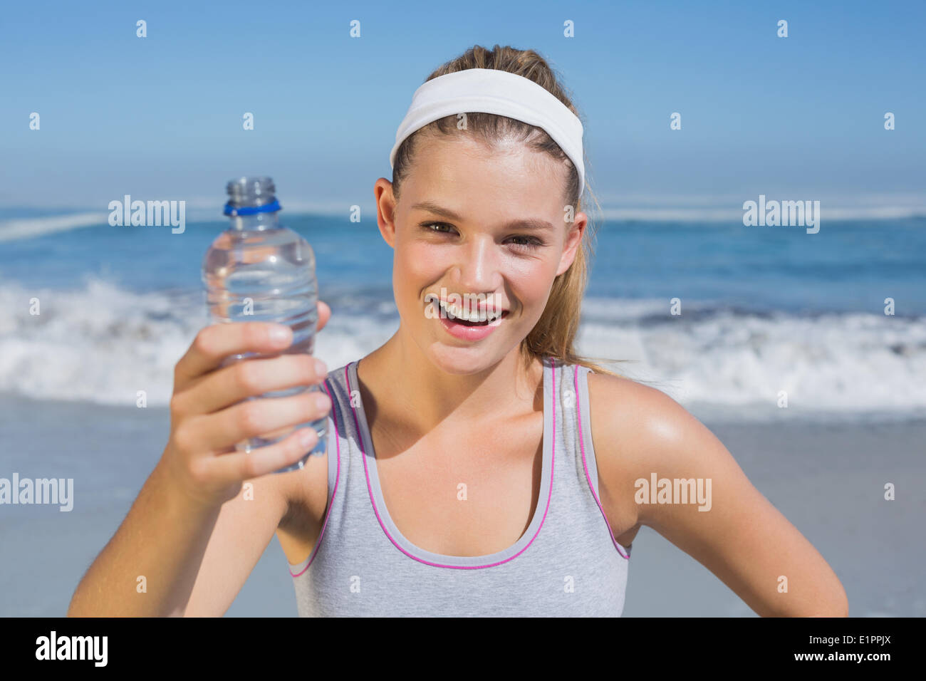 Smiling blonde sportive montrant une bouteille d'eau sur la plage Banque D'Images