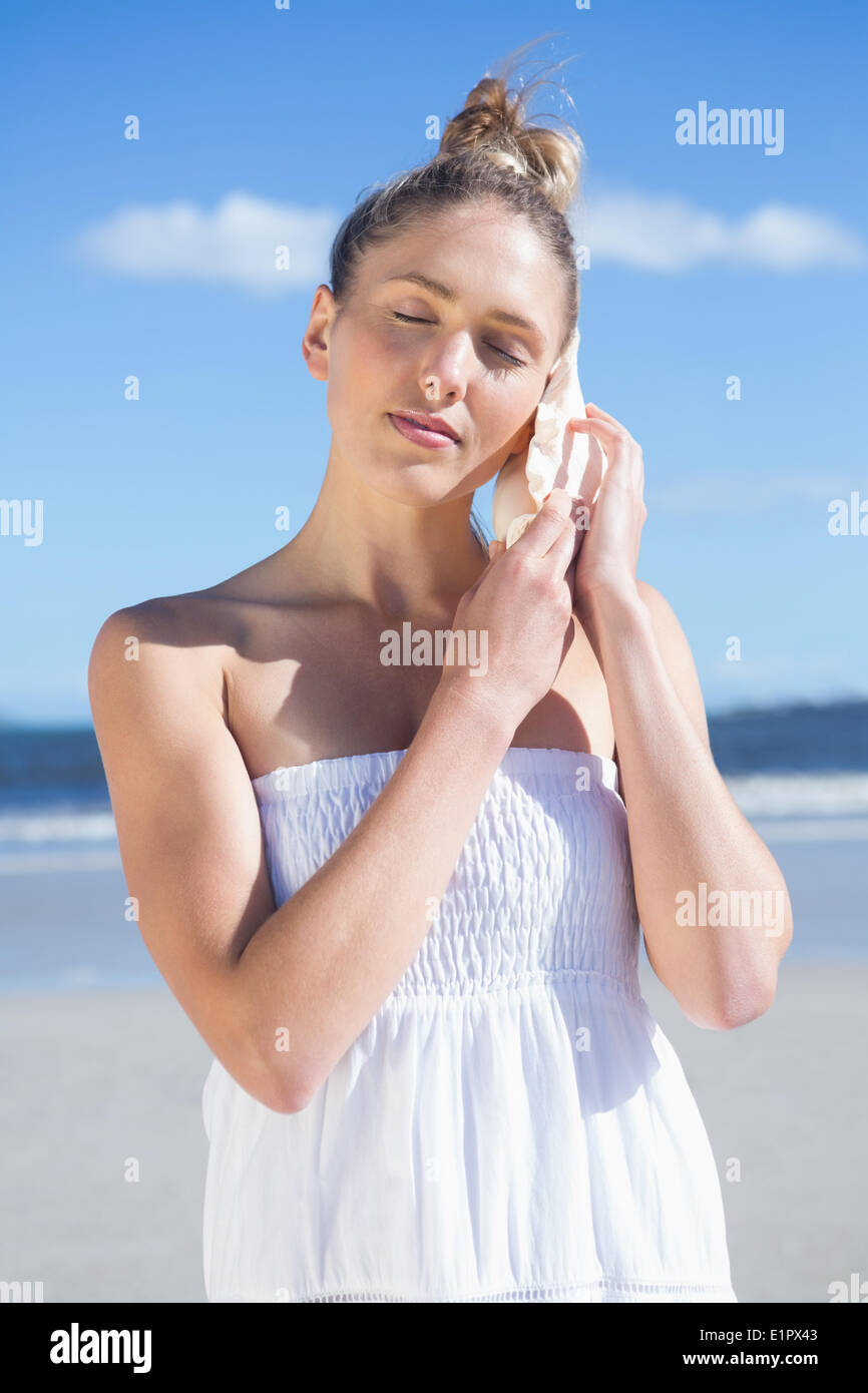 Jolie blonde en robe blanche à écouter sur la plage de la conque Banque D'Images