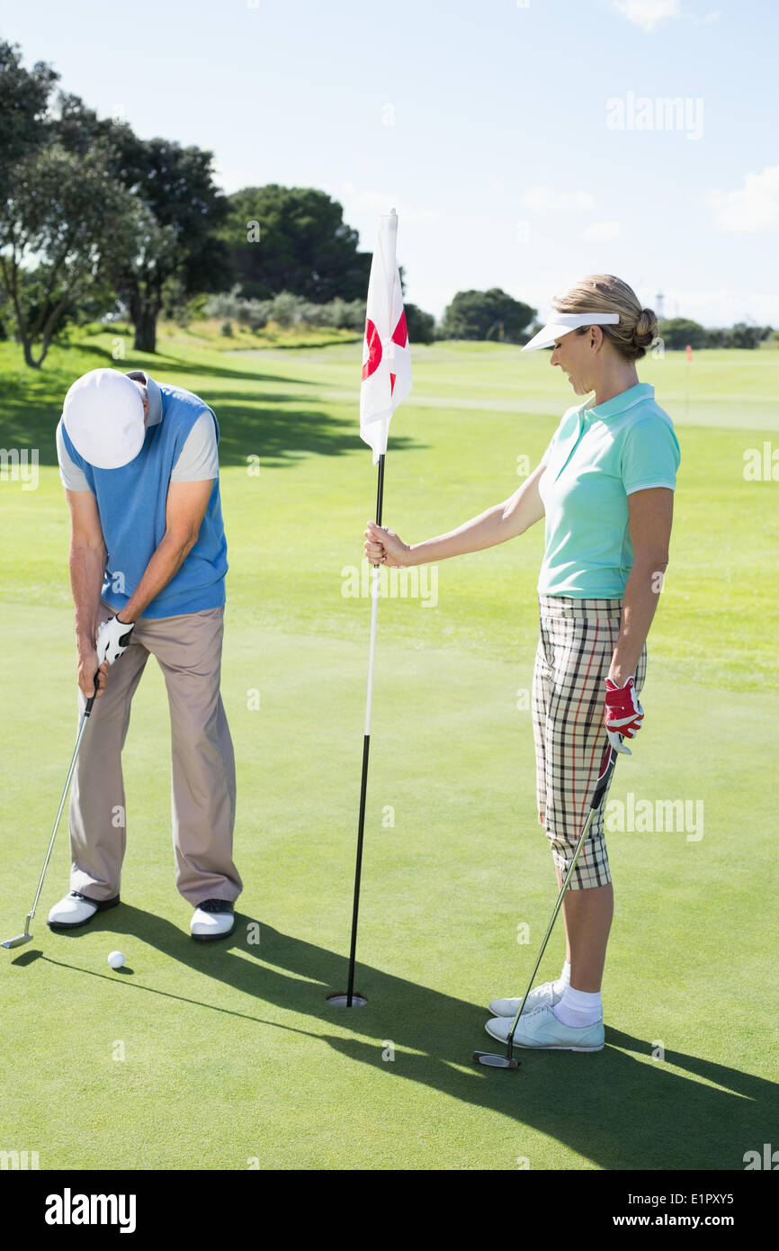 Dix-huitième holding golfeur dame drapeau trou pour mettre partenaire ball Banque D'Images