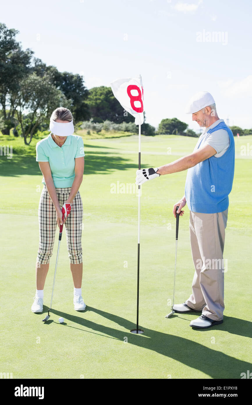 Dix-huitième holding golfeur drapeau trou pour mettre partenaire ball Banque D'Images