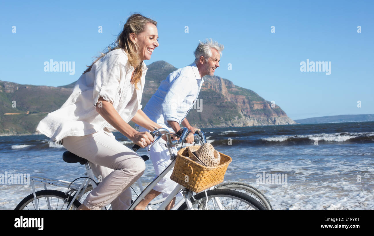 Smiling couple équitation leurs vélos sur la plage Banque D'Images