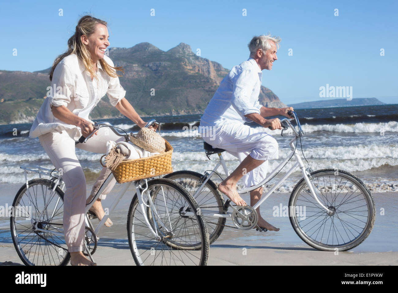 Smiling couple équitation leurs vélos sur la plage Banque D'Images