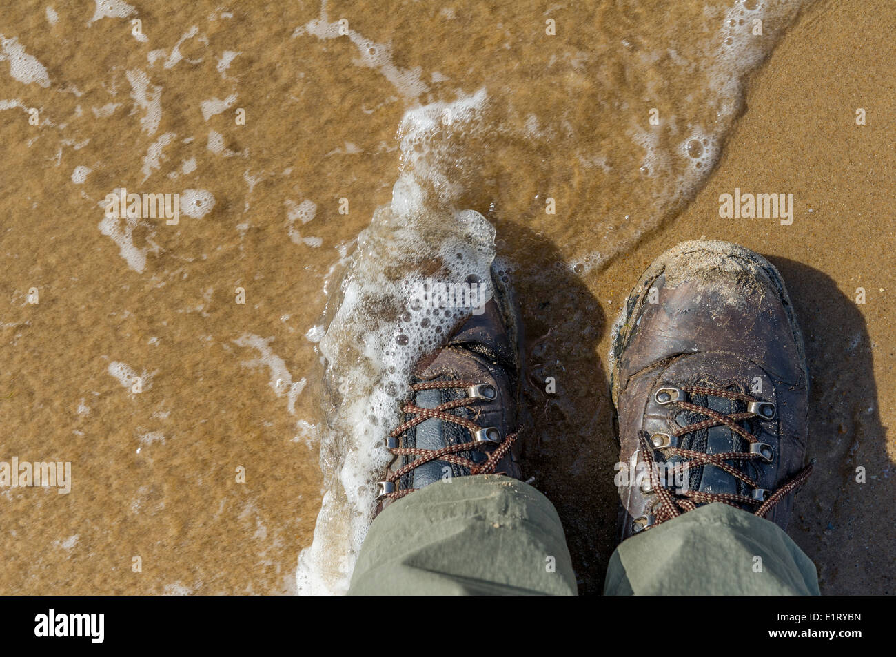 Un homme portant des bottes soit mouillé par la marée montante. Banque D'Images