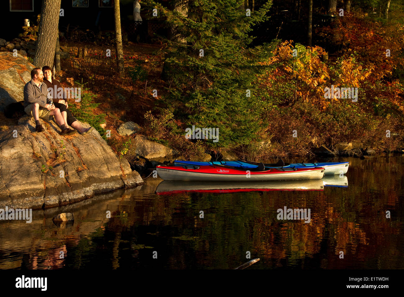 Middle-aged couple profiter matin calme sur des rochers près de leur petite maison avec des kayaks, Source Lake, Algonquin Park, Ontario, Canada Banque D'Images