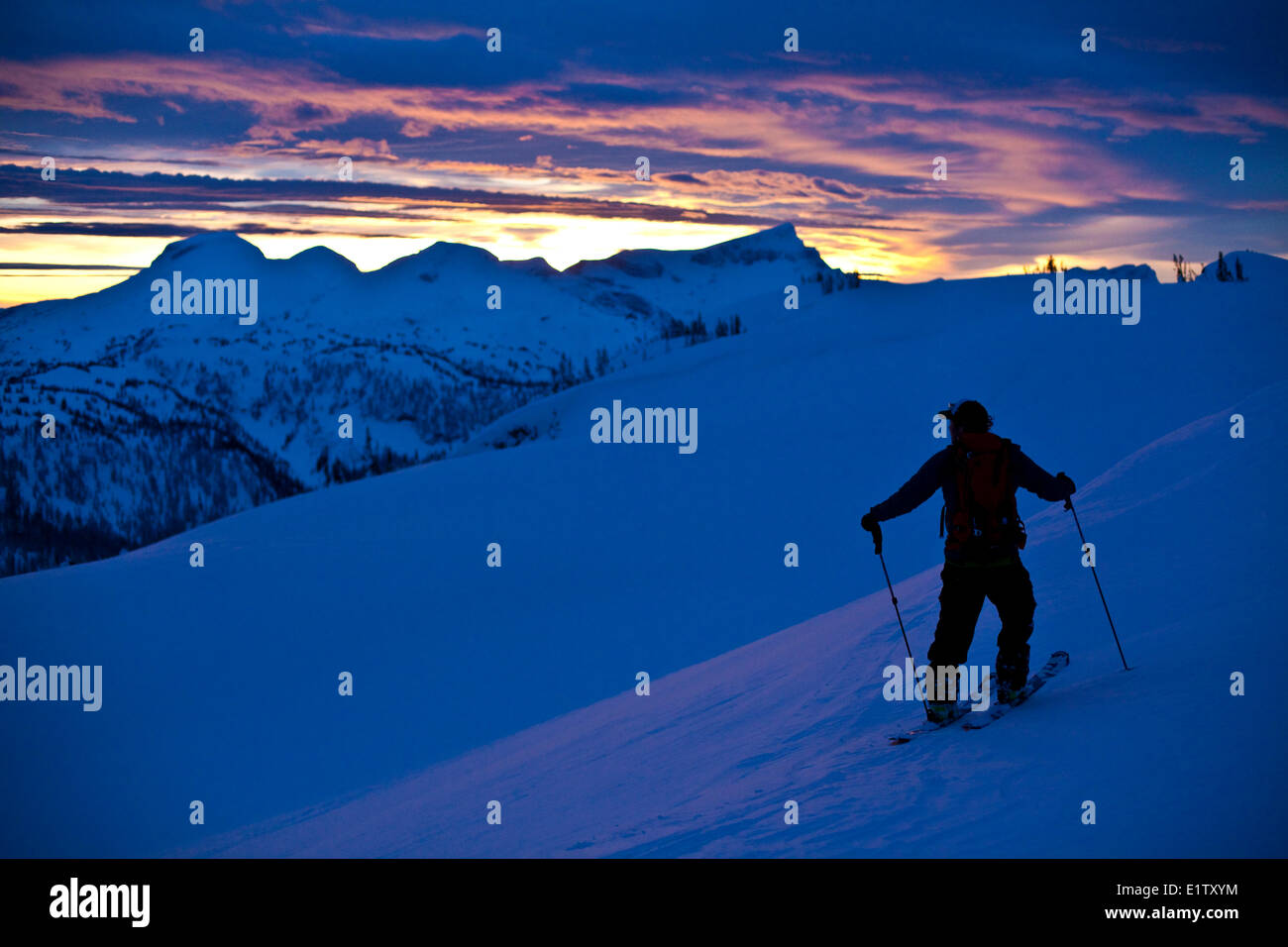 Un skieur d'arrière-pays prend un moment pour admirer le coucher du soleil au sol, l'arrière-pays de montagnes Monashee, Revelstoke, BC Banque D'Images
