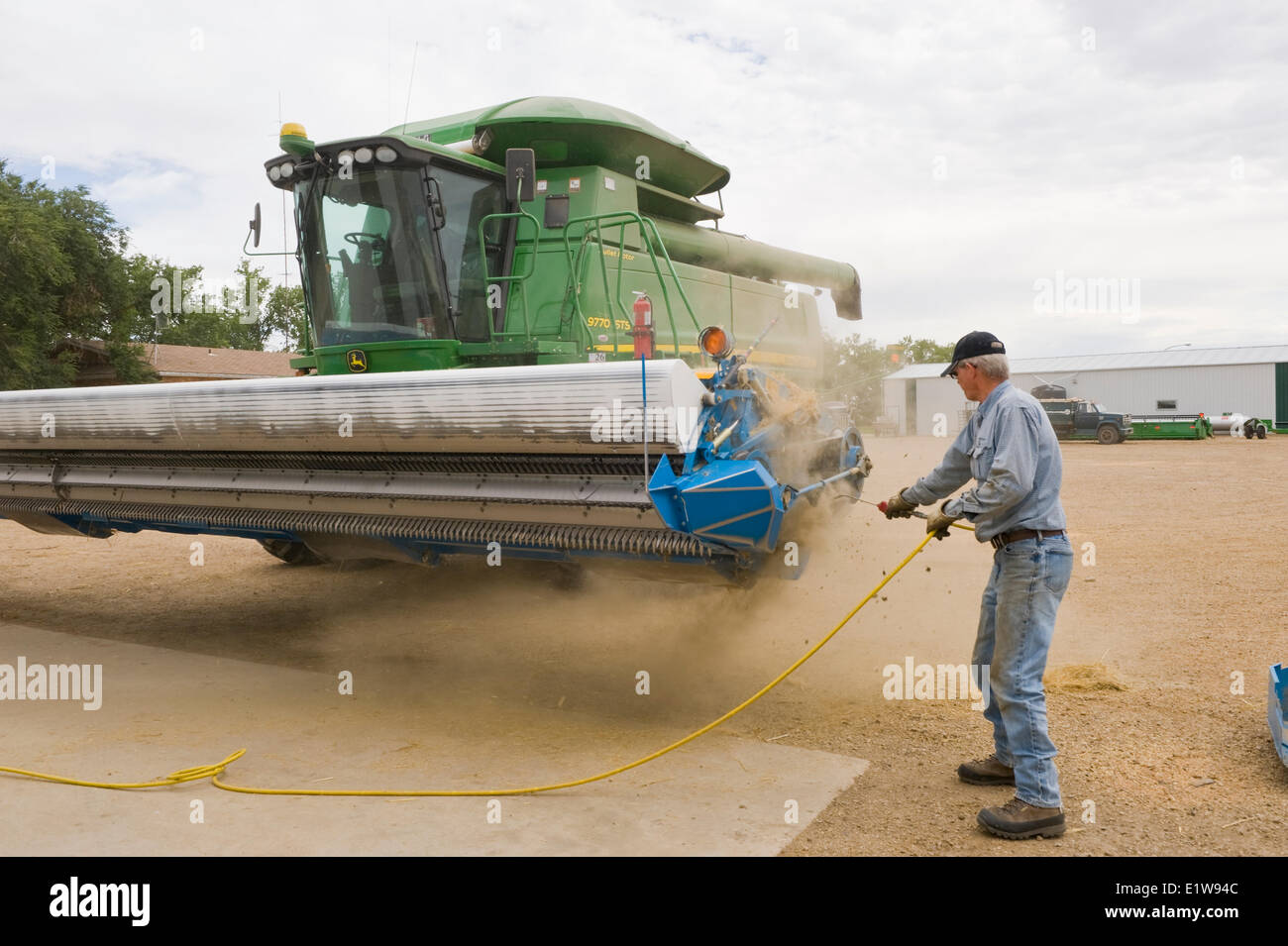 L'orge agriculteur nettoie les débris d'un racleur de coupe sur une moissonneuse-batteuse stationnée dans sa ferme, près de Ponteix, Saskatchewan, Canada Banque D'Images