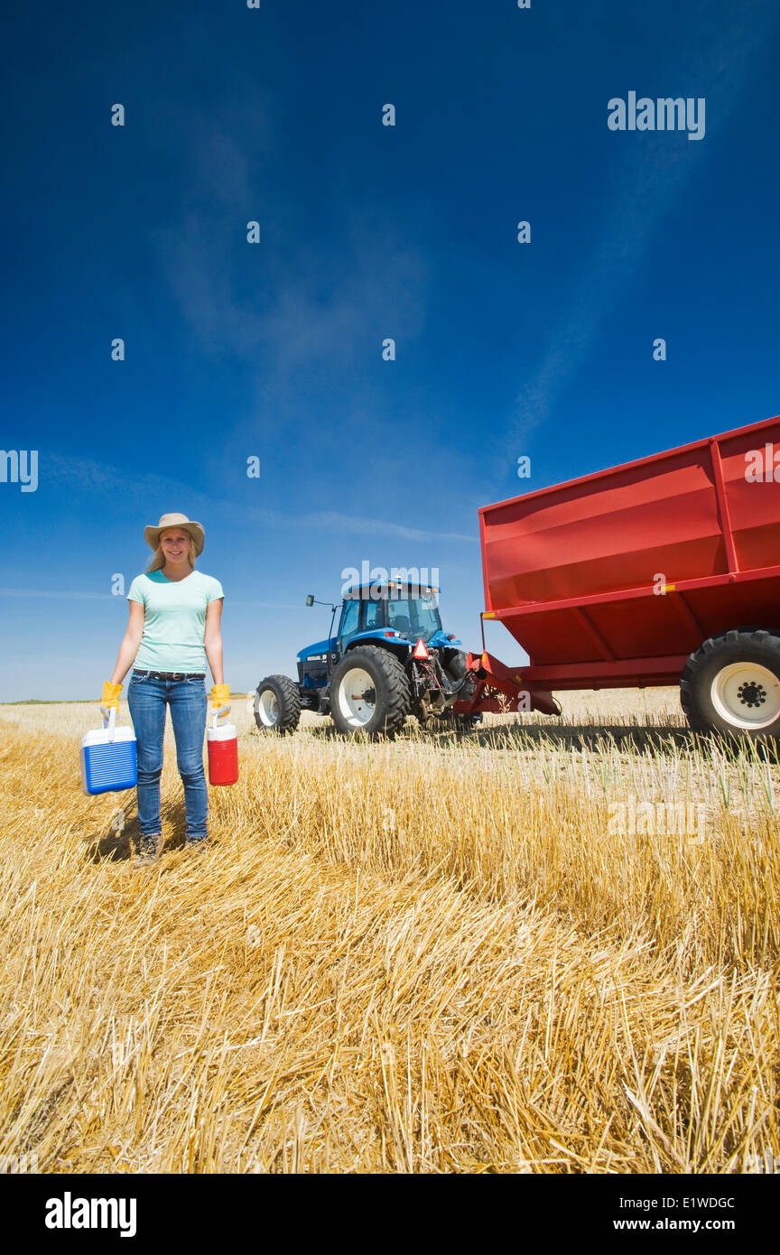 Une ferme Girl standing in chaume dans l'avoine avant d'un tracteur et chariot à grain pendant la récolte, près de Dugald (Manitoba), Canada Banque D'Images