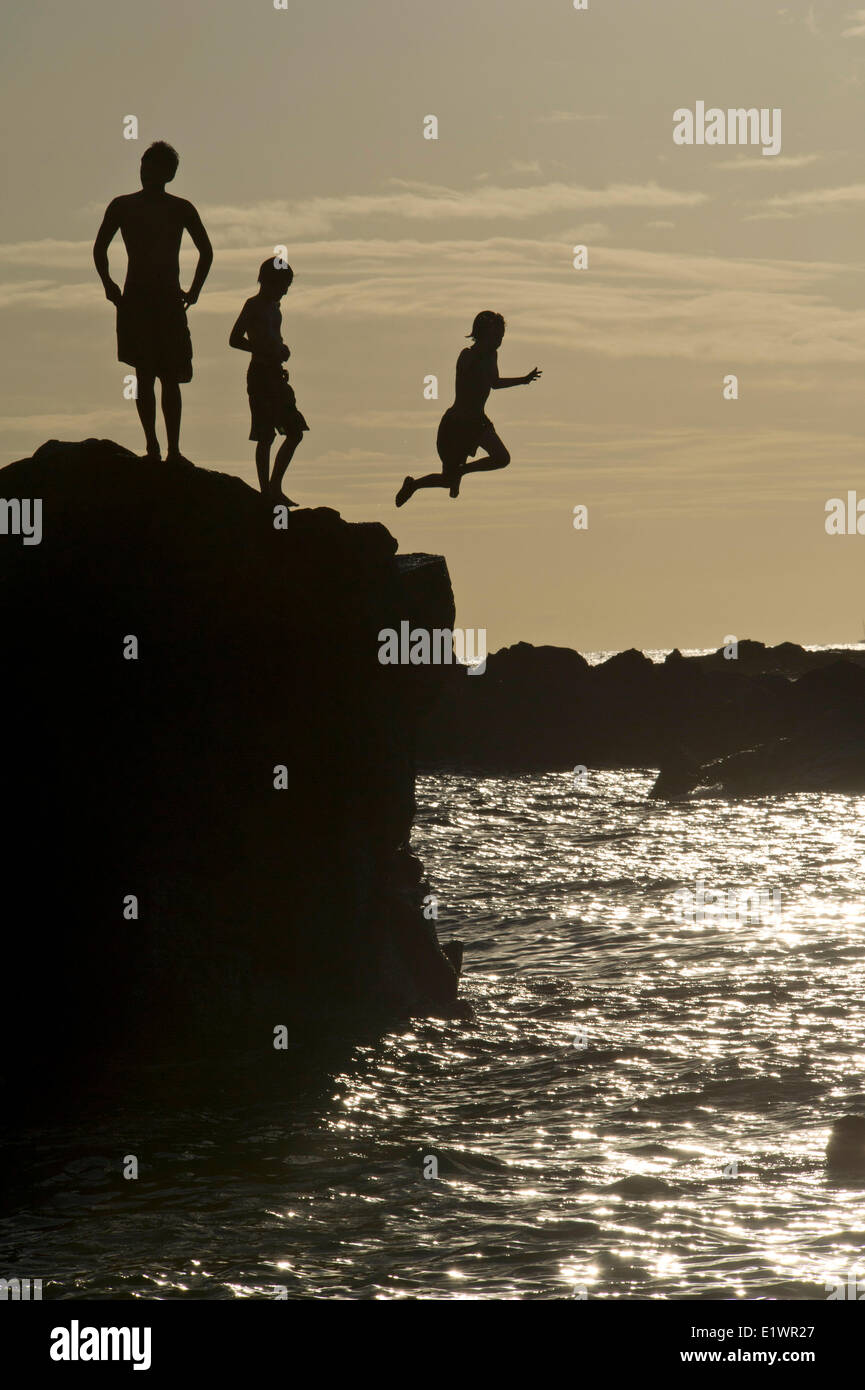 Saut de la jeunesse de la roche dans la mer au coucher du soleil Banque D'Images