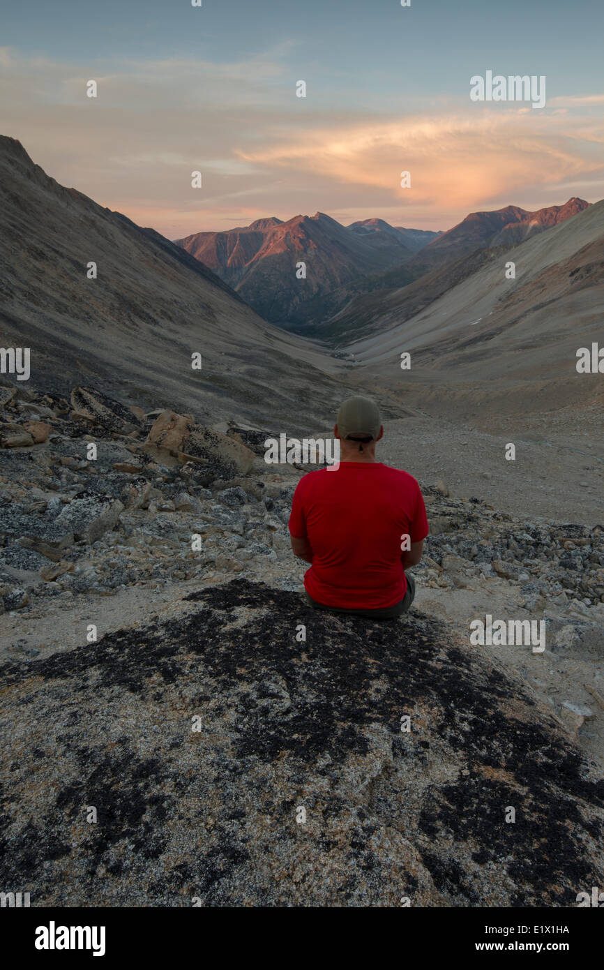 Homme est assis sur un rocher au coucher du soleil avec vue sur Jone's Pass à Carcross (Yukon). Banque D'Images