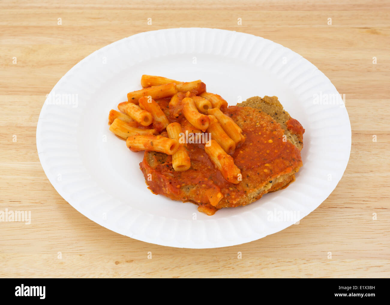 Un plat cuisiné le dîner de bouchées de poulet avec une sauce tomate et des pâtes sur une assiette en carton sur une table en bois. Banque D'Images