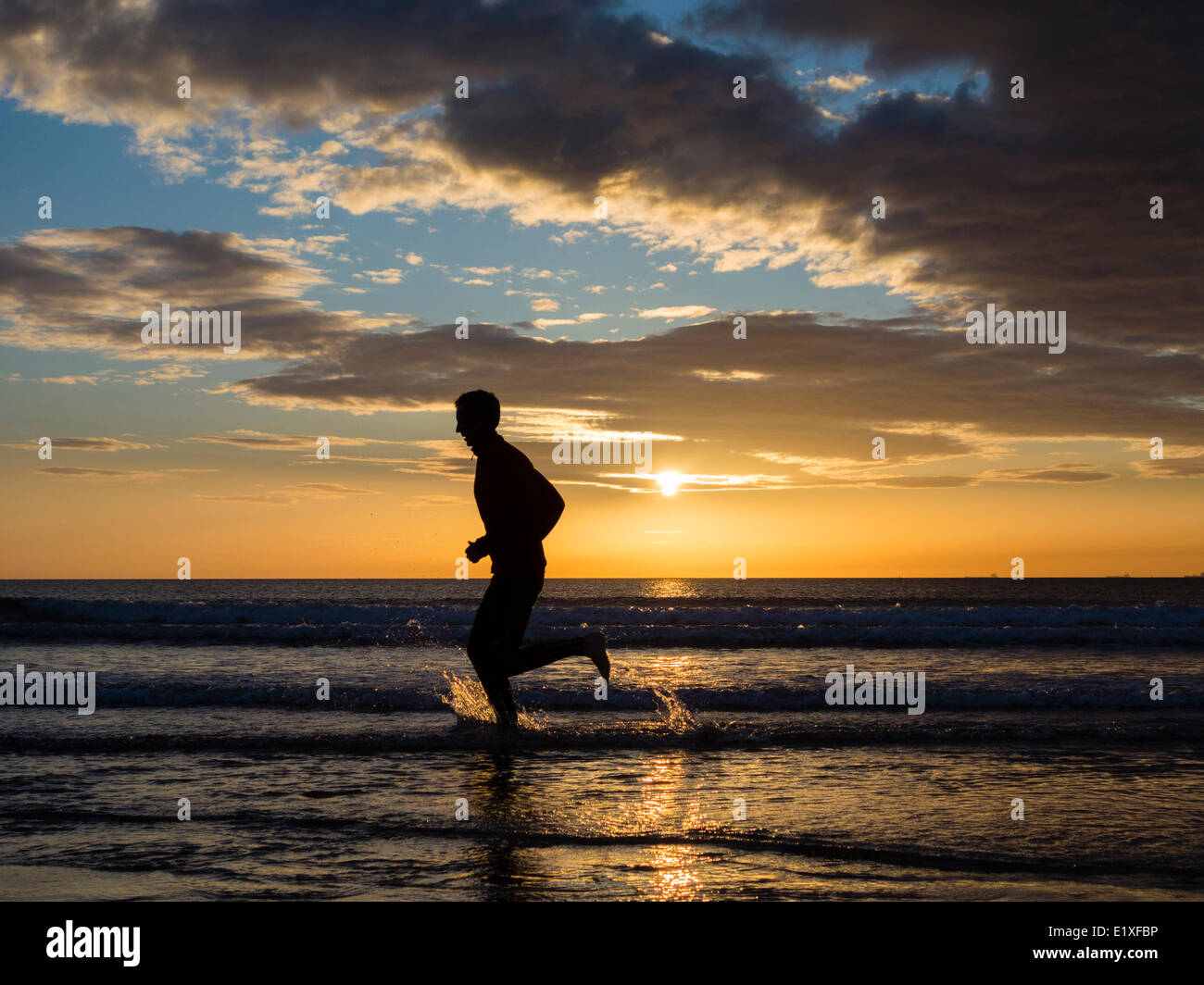 Jogger en marche pieds nus dans la mer au lever du soleil. UK Banque D'Images