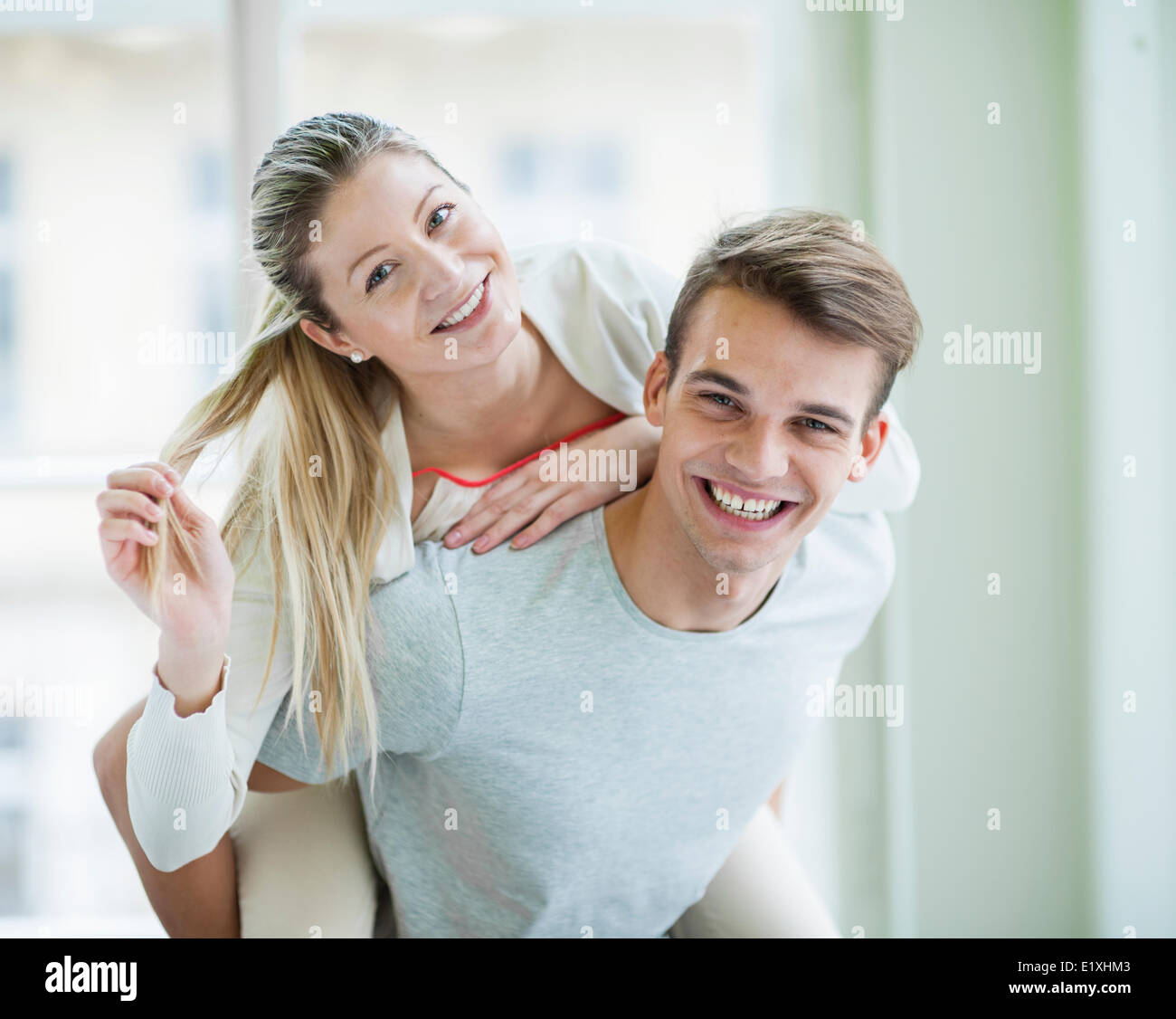 Portrait of happy young man giving piggyback ride to woman at home Banque D'Images