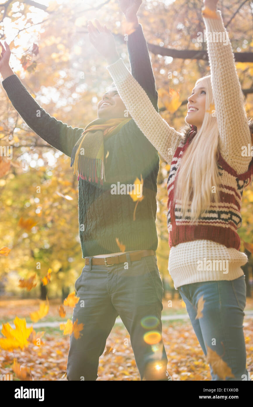 Happy young couple with arms raised profitant de la chute des feuilles d'automne dans le parc Banque D'Images