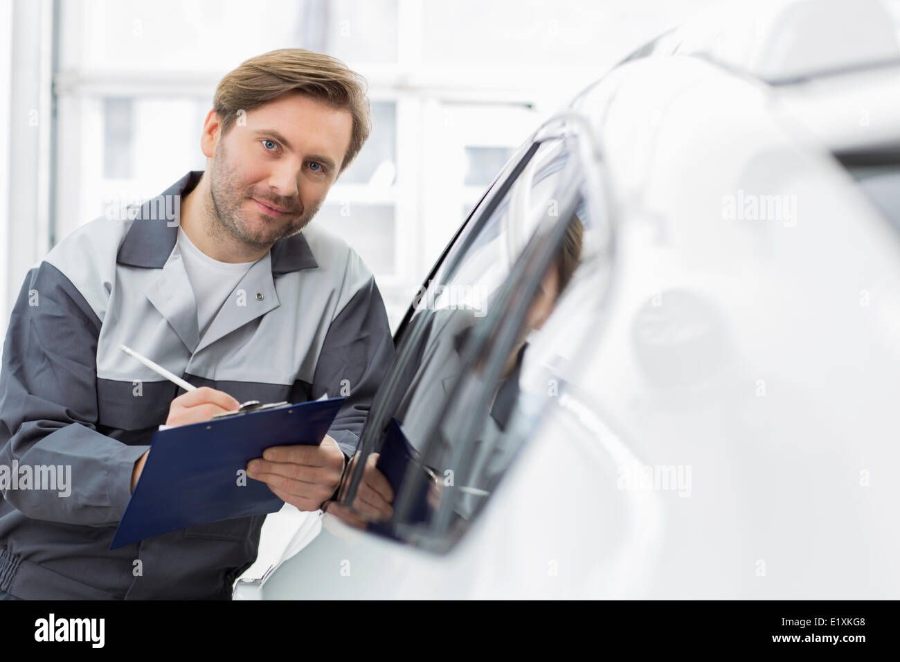 Portrait of smiling woman holding clipboard mécanicien automobile tout en s'appuyant sur la fenêtre de voiture en atelier Banque D'Images
