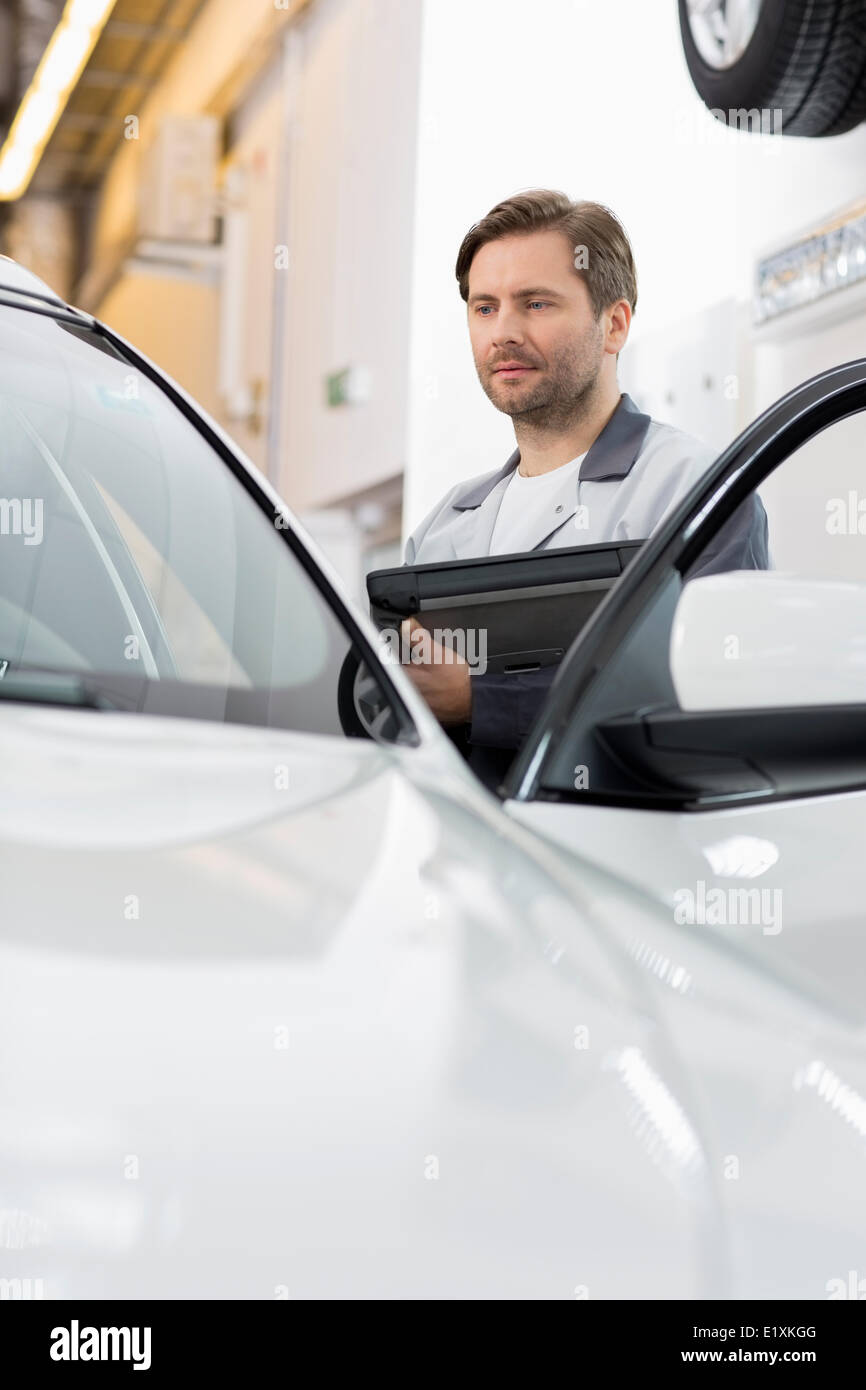 Ingénieur Maintenance holding tablet PC lors de l'examen de voiture dans l'atelier de réparation Banque D'Images