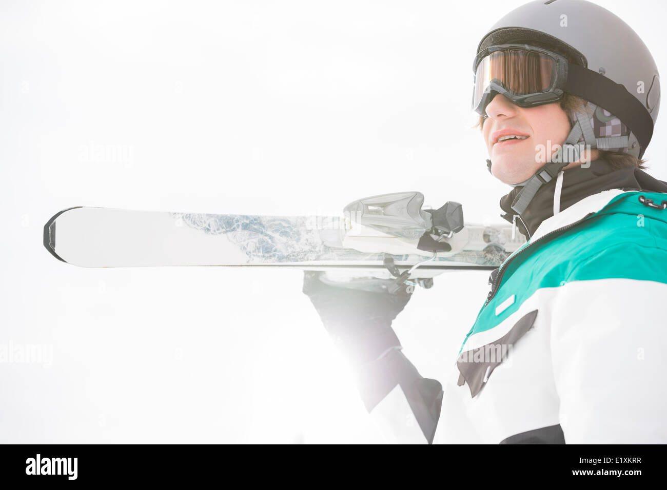 Smiling young man carrying skis contre ciel clair Banque D'Images