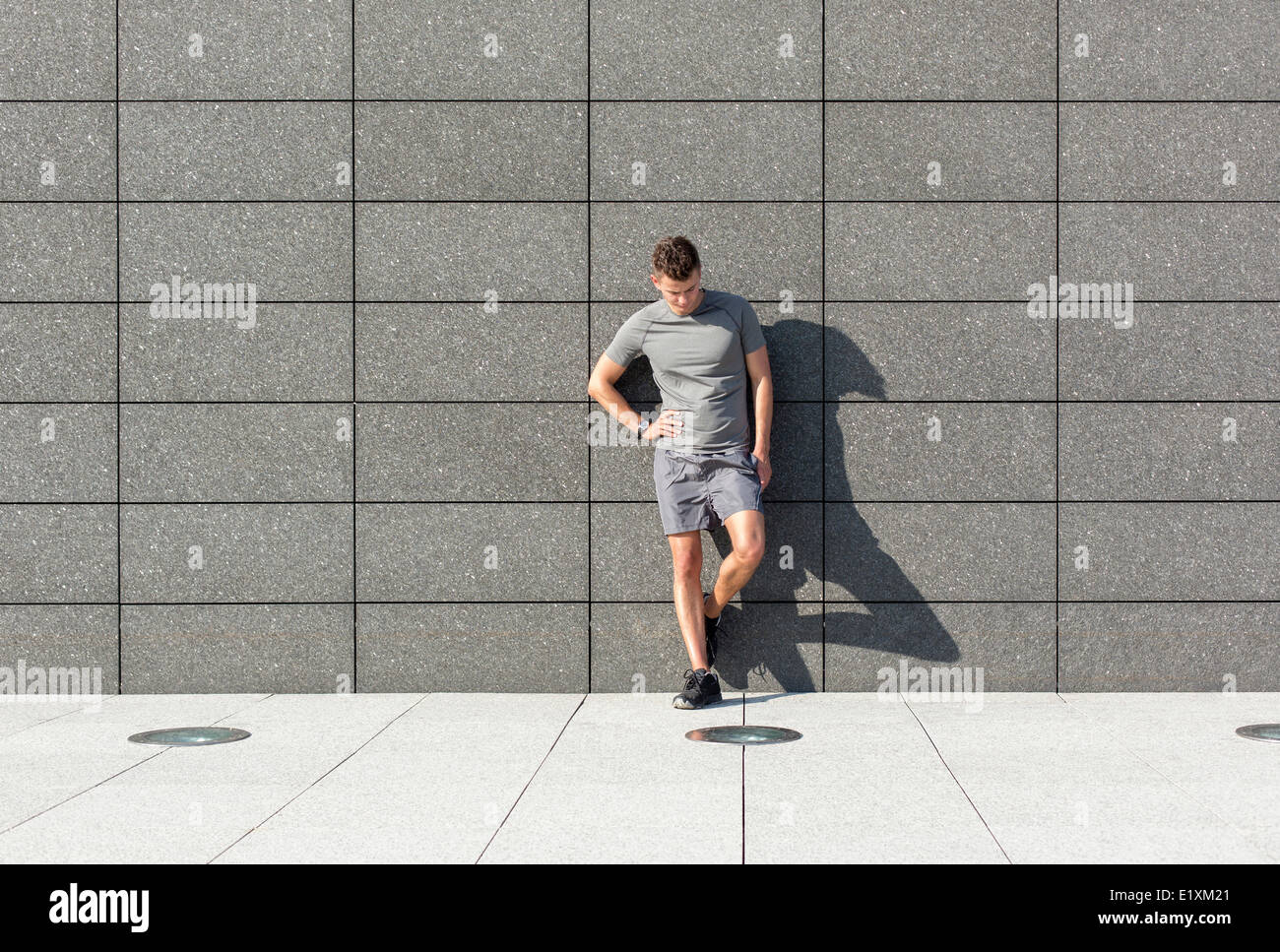 Toute la longueur de fatigué sporty man leaning on mur carrelé Banque D'Images