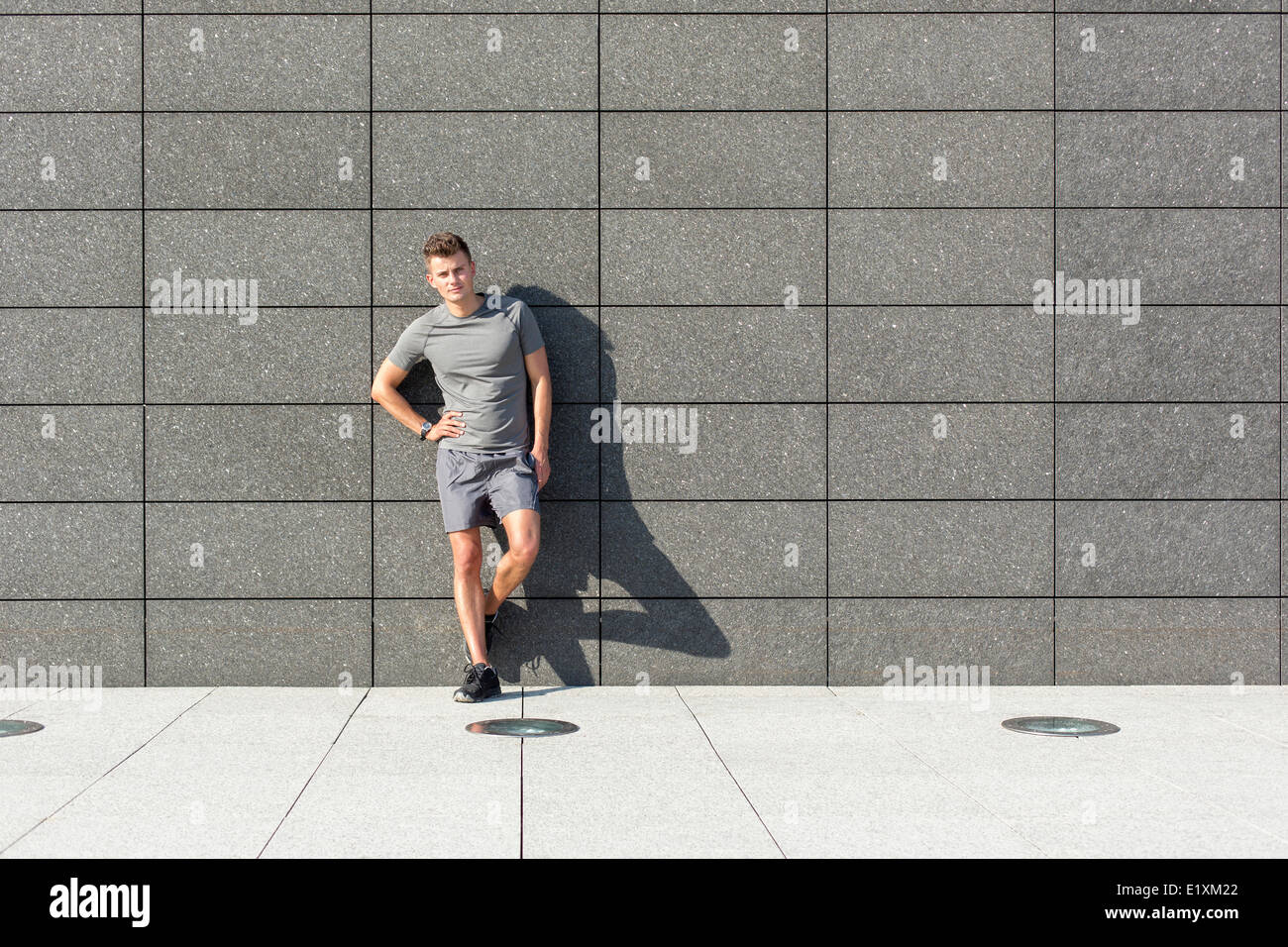Portrait of confident sporty man leaning on mur carrelé Banque D'Images