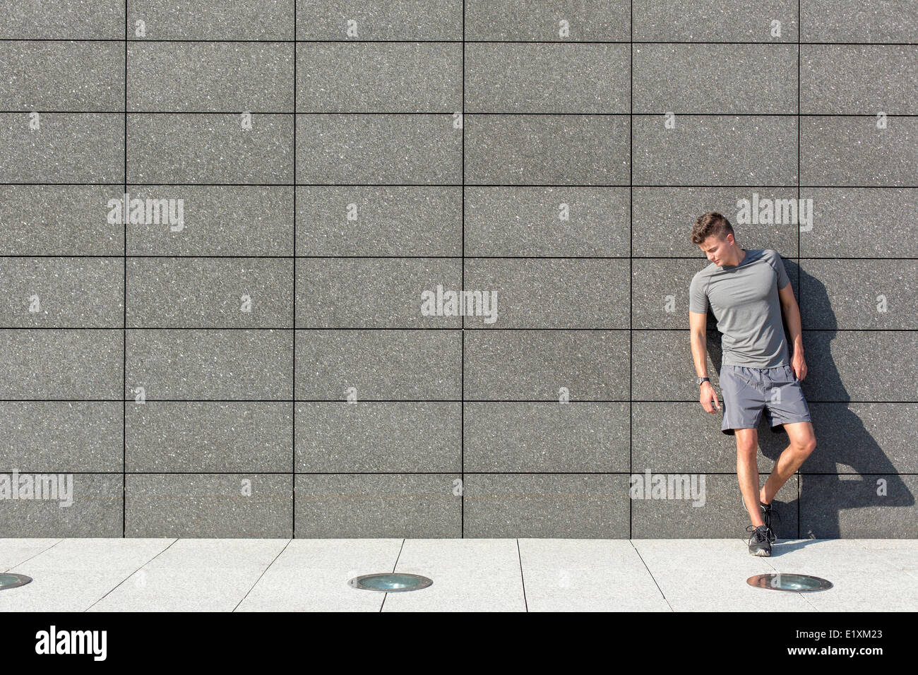 Toute la longueur de fatigué sporty man leaning on mur carrelé Banque D'Images