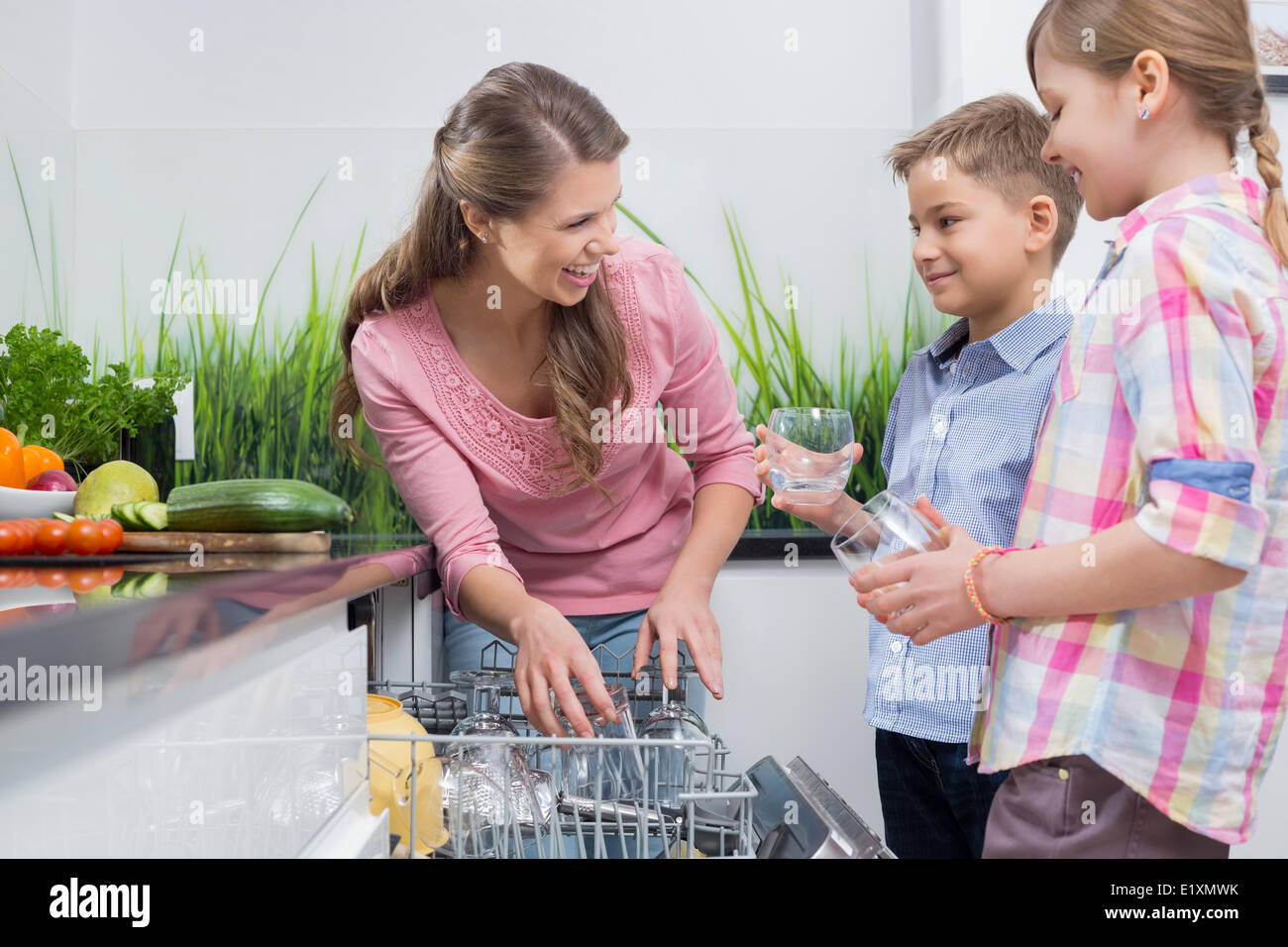 La mère et les enfants heureux de placer dans le lave-vaisselle verres Banque D'Images