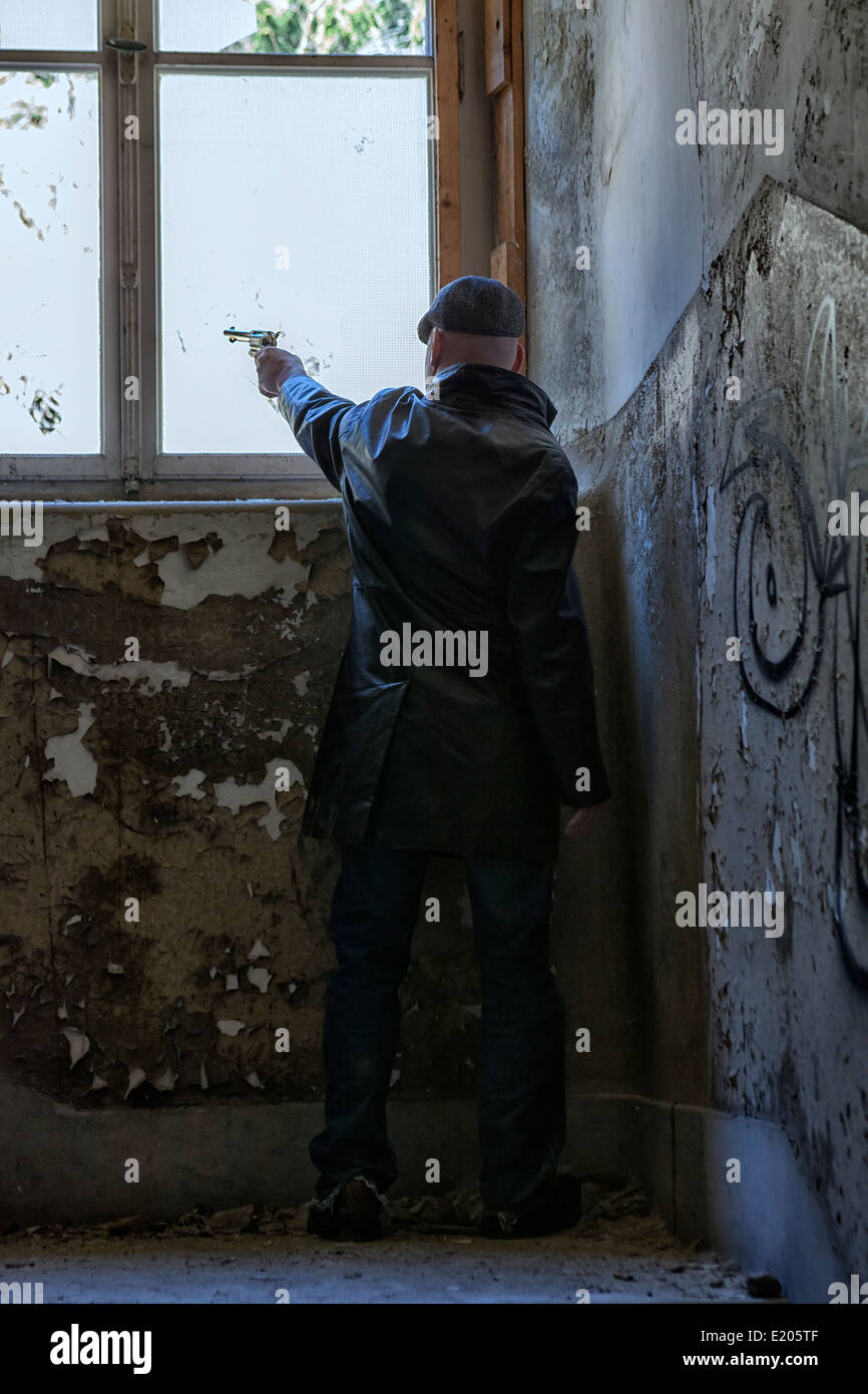 Un homme en vêtements sombres est une fenêtre de tir dans un vieux bâtiment abandonné Banque D'Images