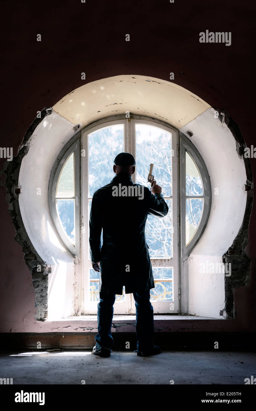 Un homme avec une arme à feu en face d'une ancienne fenêtre dans un immeuble abandonné Banque D'Images