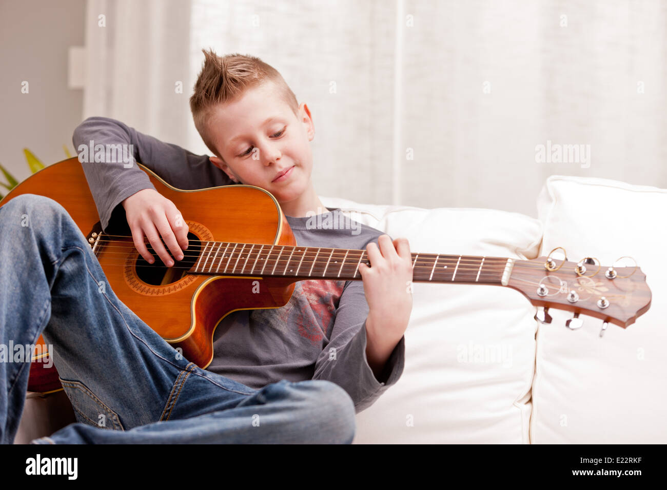 Petit garçon qui joue de la guitare sur un canapé dans son salon Banque D'Images