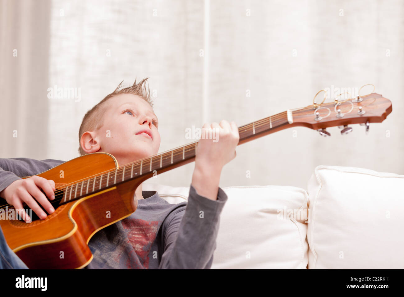 Petit garçon qui joue de la guitare sur un canapé dans son salon Banque D'Images