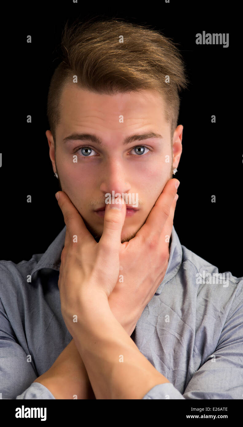 Beau jeune homme blond, l'expression grave les mains jointes devant la bouche Banque D'Images