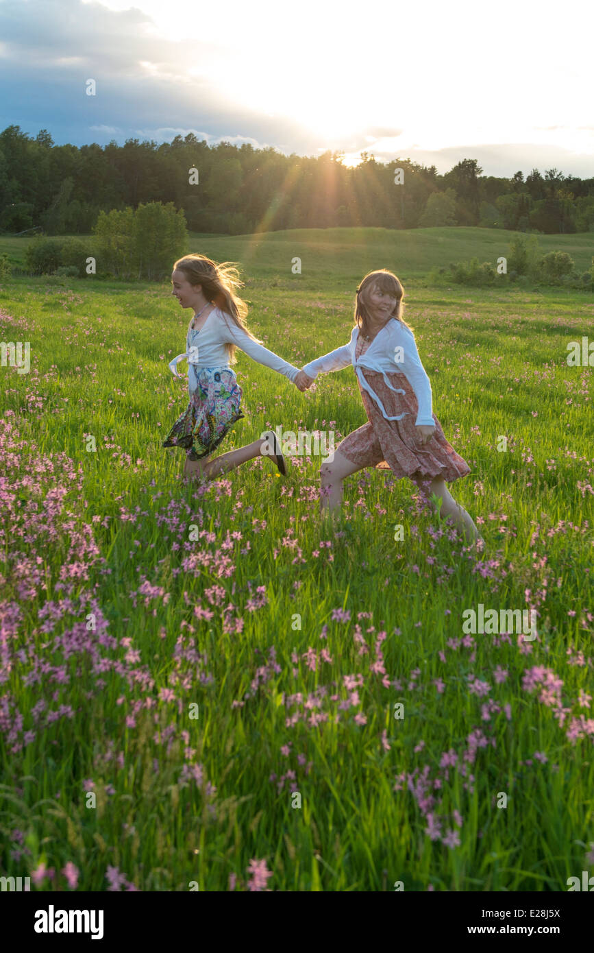 Deux adolescentes s'exécutant dans un champ de fleur au coucher du soleil. De vrais amis dans la vie réelle, ils expriment un pur bonheur. Banque D'Images