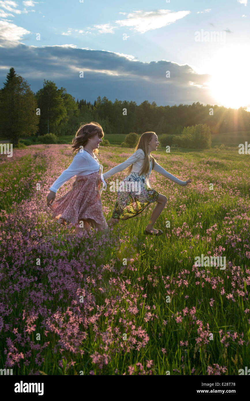 Deux adolescentes s'exécutant dans un champ de fleur au coucher du soleil. De vrais amis dans la vie réelle, ils expriment un pur bonheur. Banque D'Images