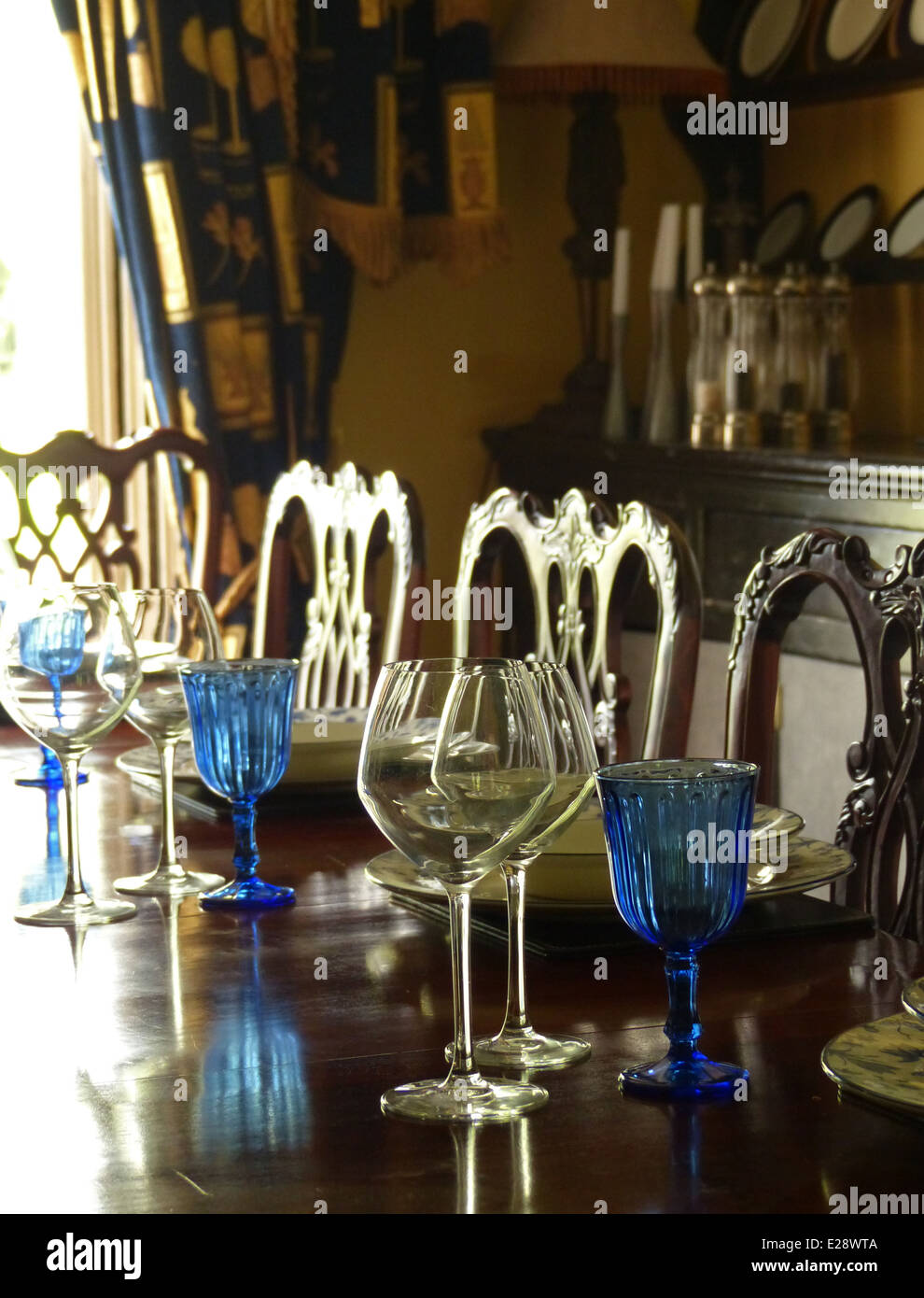 Une table à manger en bois brillant avec des assiettes et verres, y compris les verres bleus. Banque D'Images