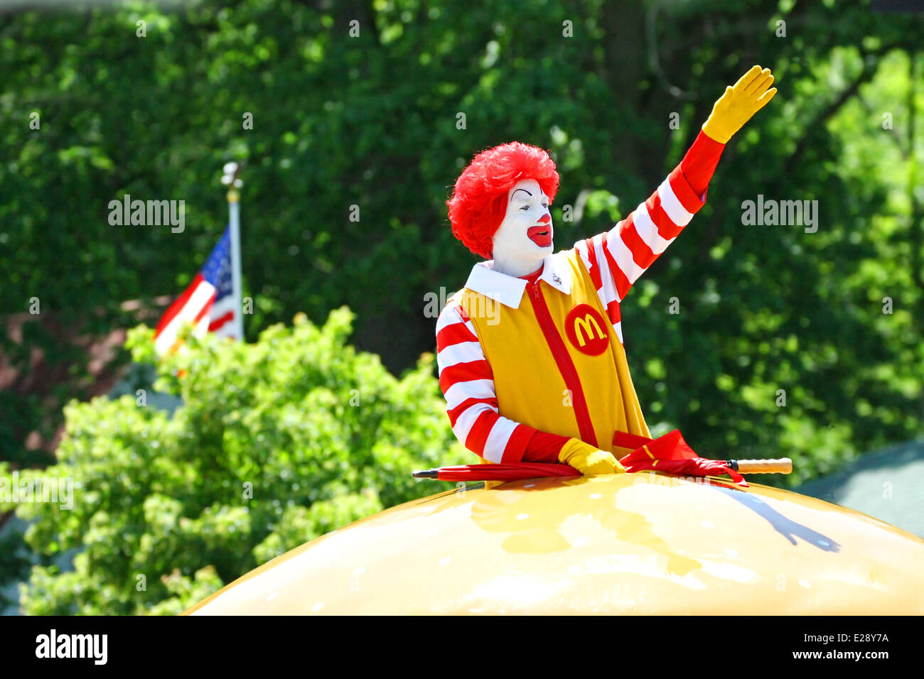 Un homme habillé en costume de Ronald McDonald est forme à la foule dans une petite ville parade. Un drapeau américain en arrière-plan Banque D'Images