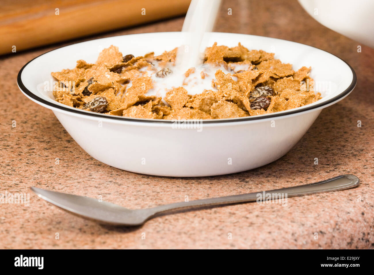 L'on verse du lait dans un bol de céréales flocons de son avec des raisins secs Banque D'Images