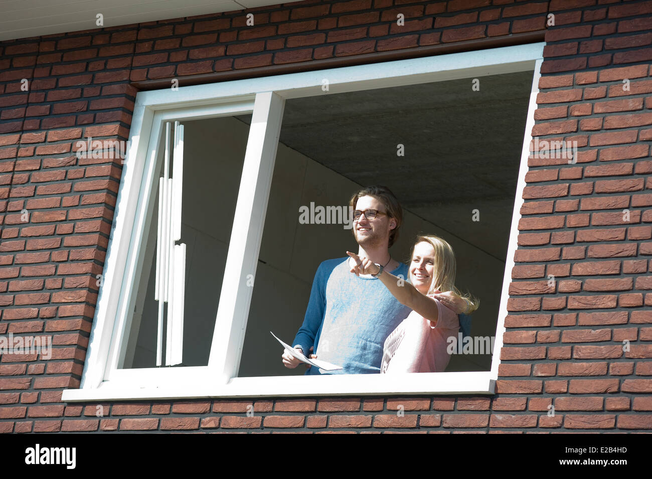 Jeune couple avec le plan directeur est à l'extérieur de la vue joyeusement de leur nouvelle maison. Banque D'Images