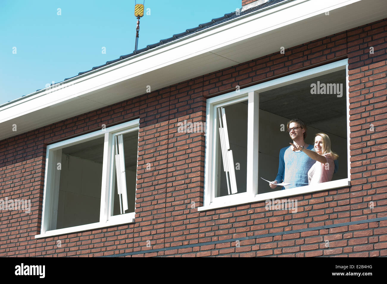 Jeune couple avec le plan directeur est à l'extérieur de la vue joyeusement de leur nouvelle maison. Banque D'Images