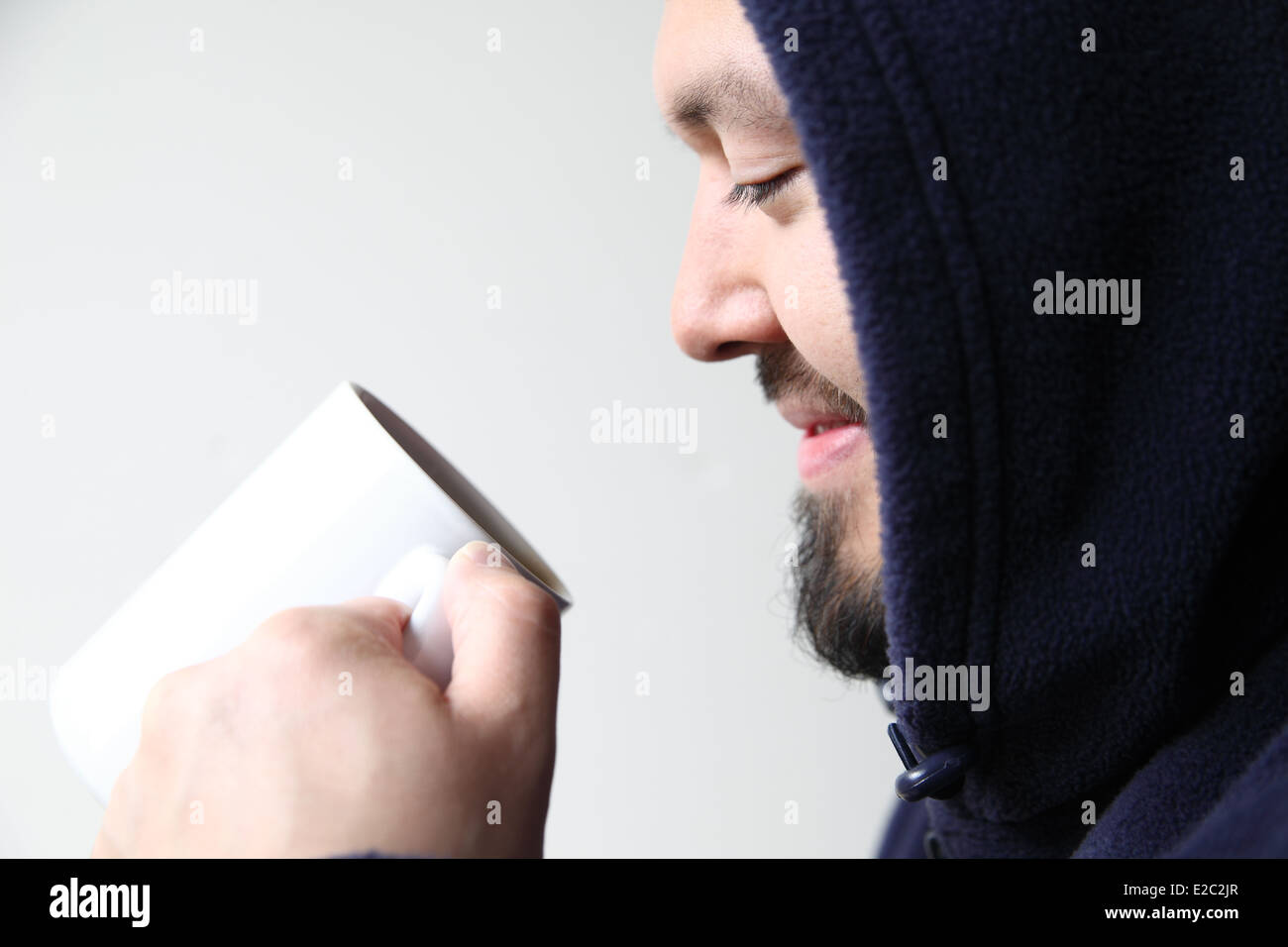 Man wearing Hooded Jacket sourit dans sa tasse de café Banque D'Images