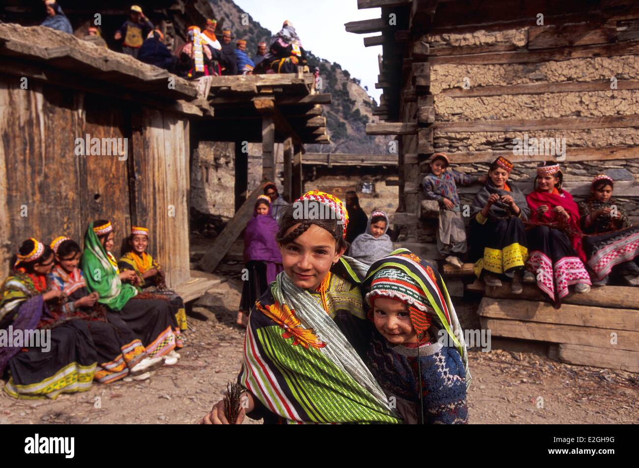 Vallées Kalash Khyber Pakhtunkhwa au Pakistan Bumburet valley alley dans village de Krakal (2150m) avec girl transportant son jeune frère et d'autres quartier de réaliser colliers aux célébrations du festival du solstice d'hiver Chaumos Banque D'Images